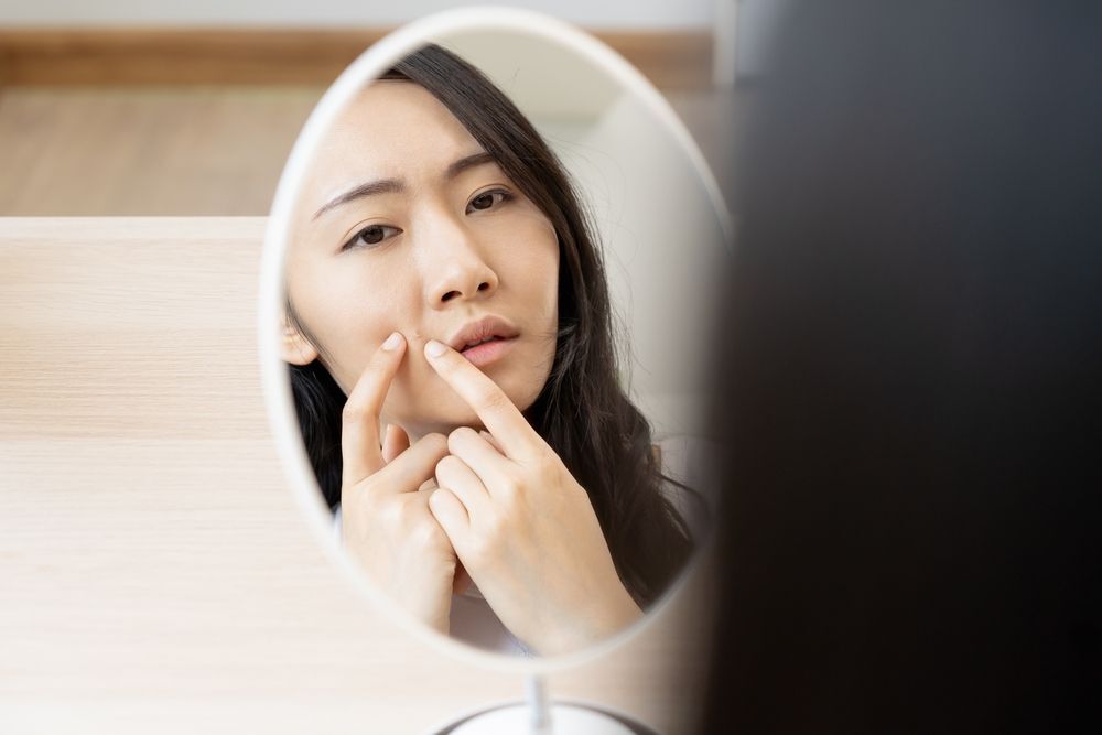 A woman squeezing her cheek in front of a mirror.