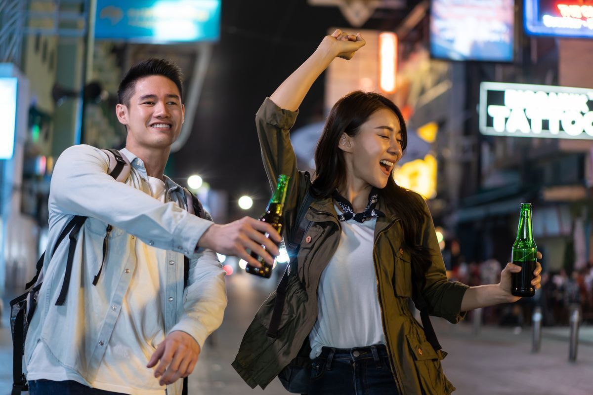 Asian man drinking alcohol while walking on street with Asian woman