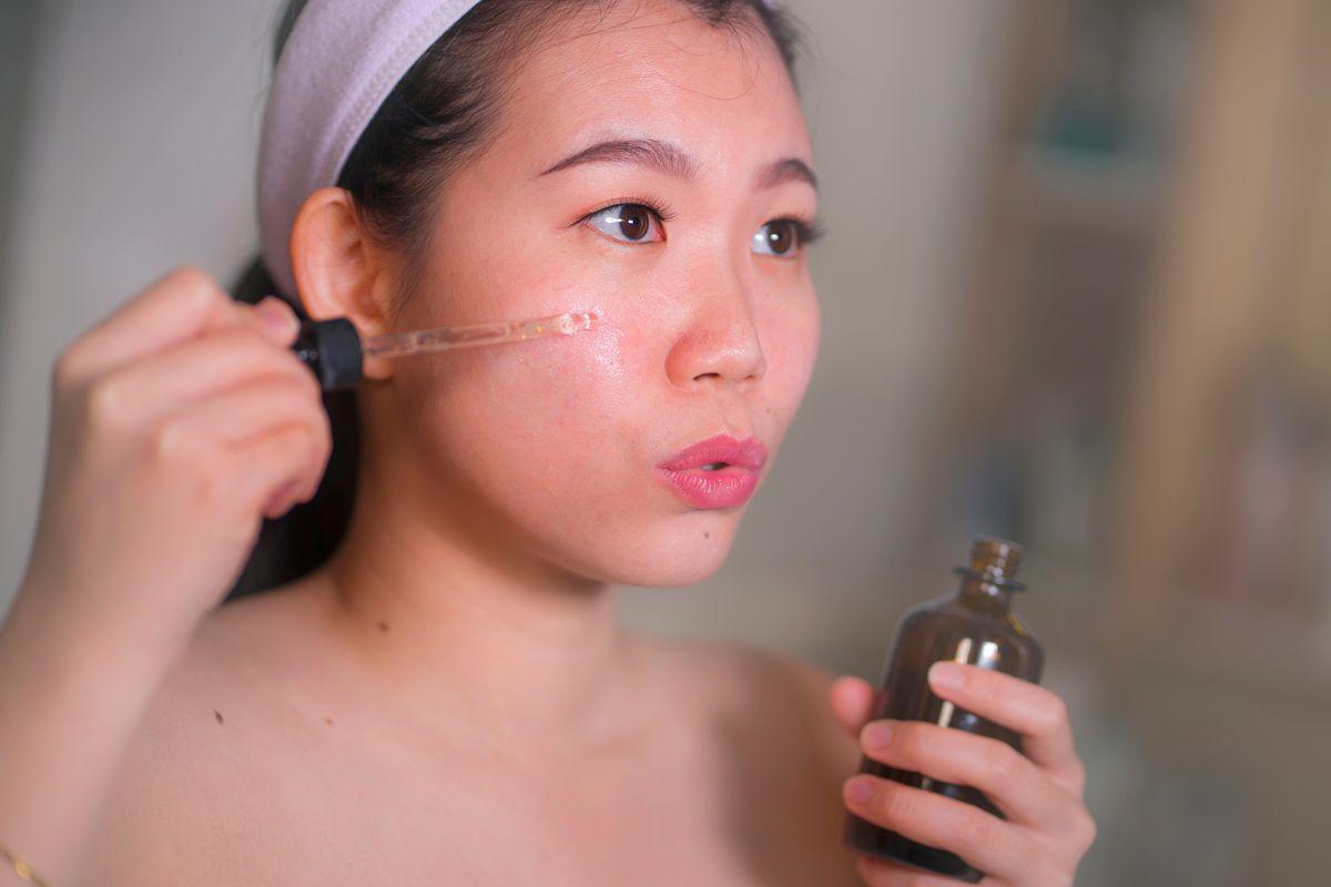 Asian woman applying serum on her cheek 