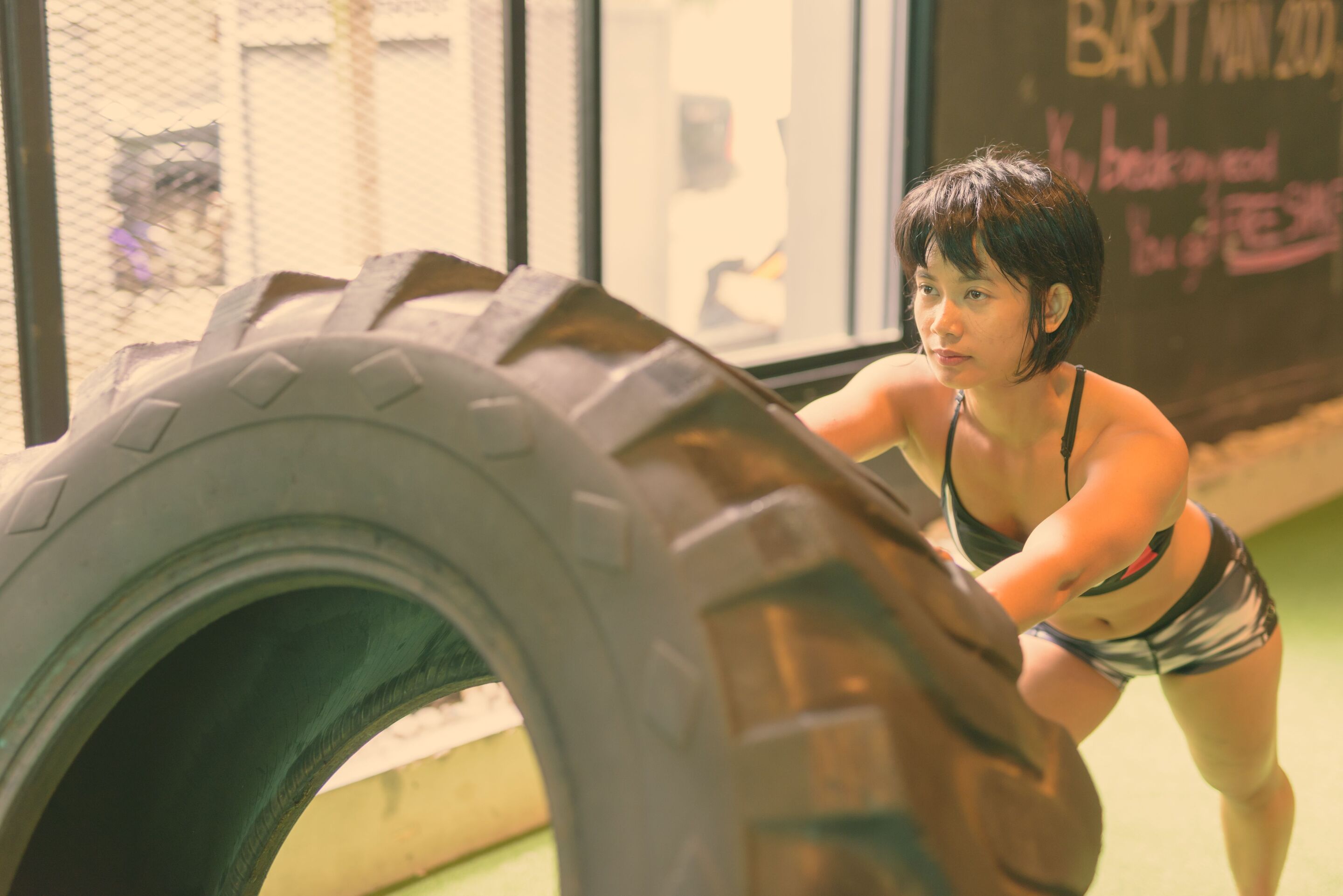 An Asian woman doing tire flips at the gym