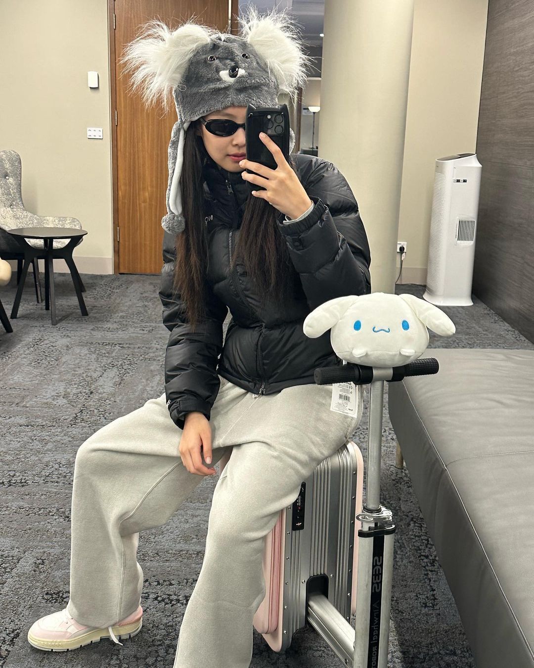 BLACKPINK’s Jennie taking a mirror selfie while wearing a puffer jacket, koala beanie, and white sweatpants.