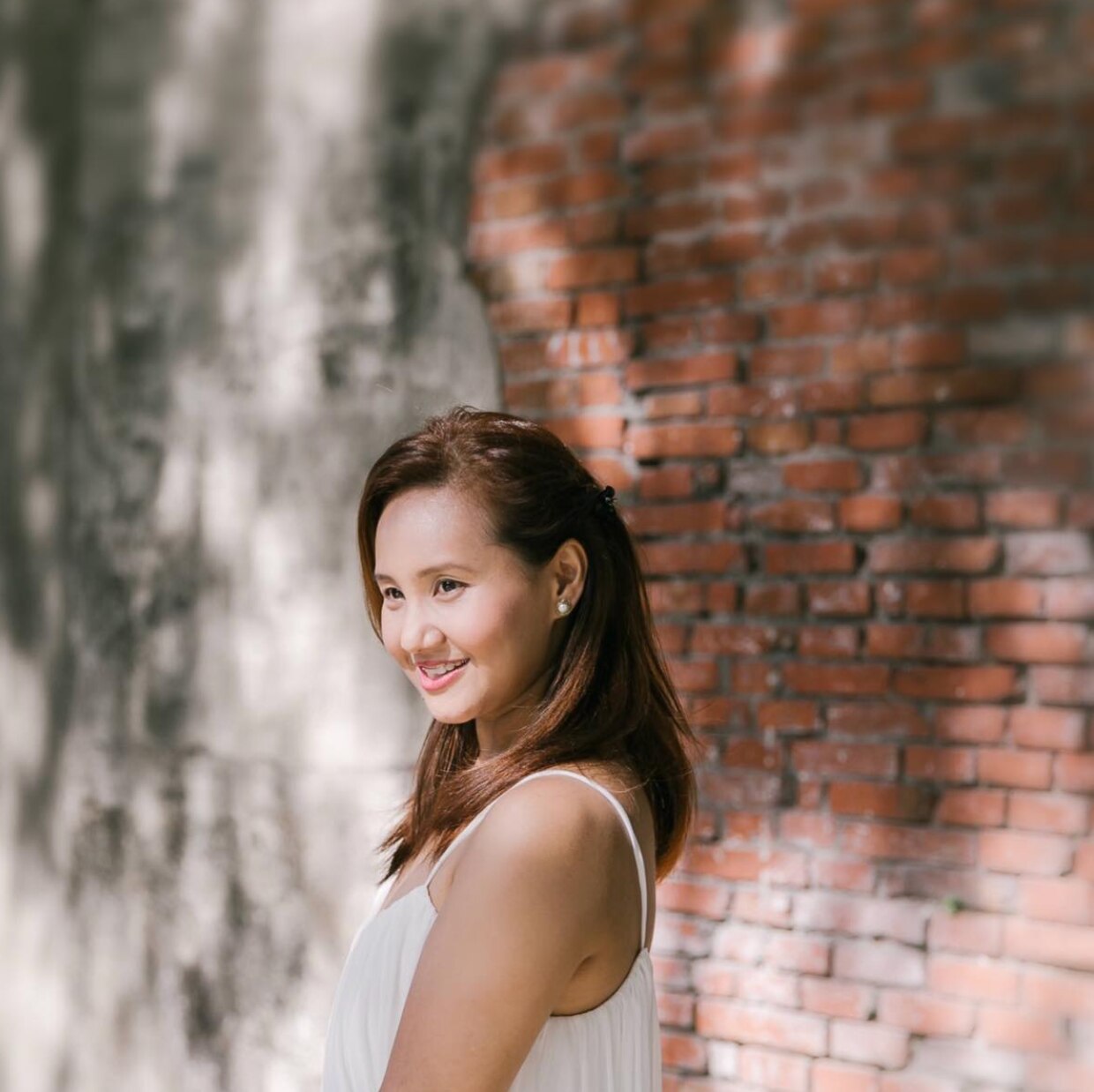 Side view of an Asian woman smiling against a brick wall.