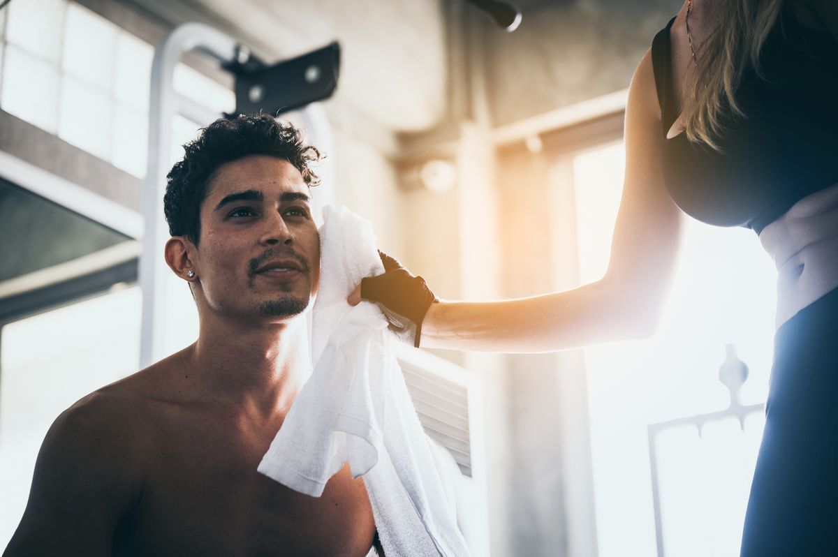 Woman wiping man’s face with a towel at the gym.