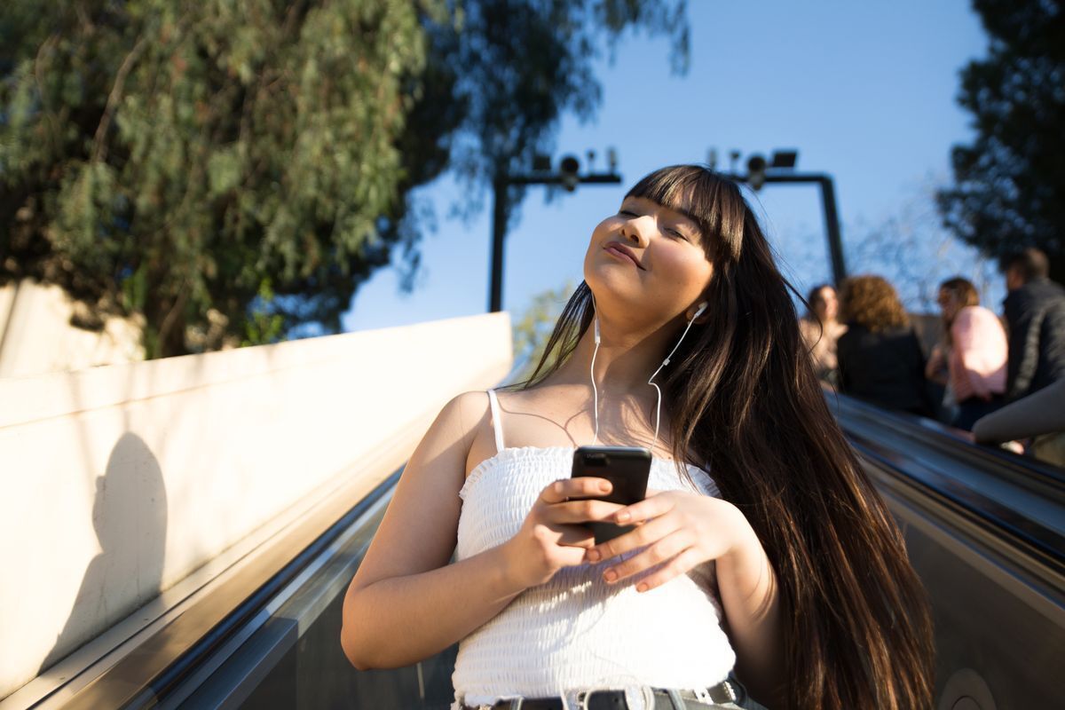 Woman with full bangs and long hair listening to music from her phone.