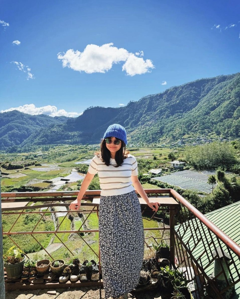 Woman in white top and maxi skirt posing in front of a mountain view.