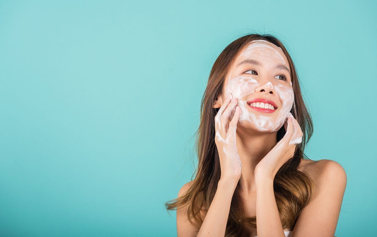 Young Asian girl applying facial foam, isolated on blue background