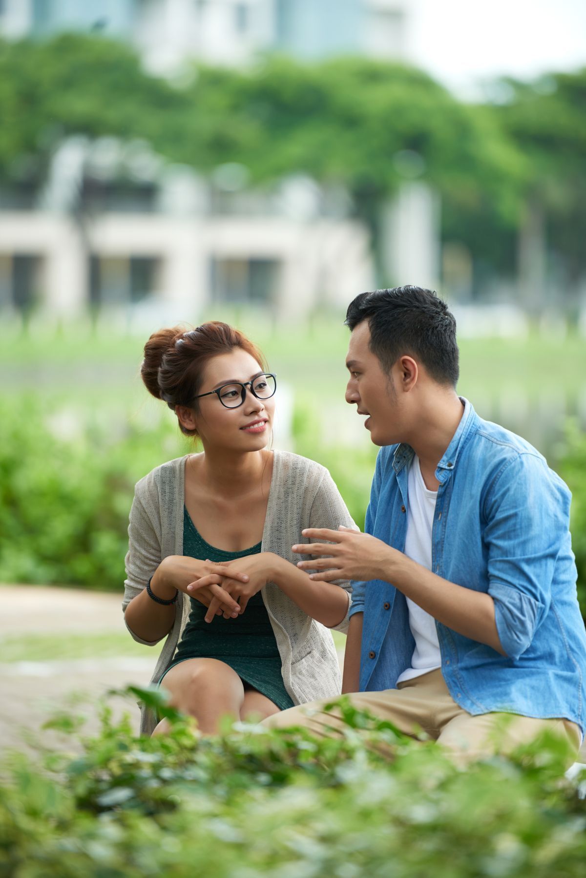 Asian man making hand gestures and woman with her hands folded talking outdoors