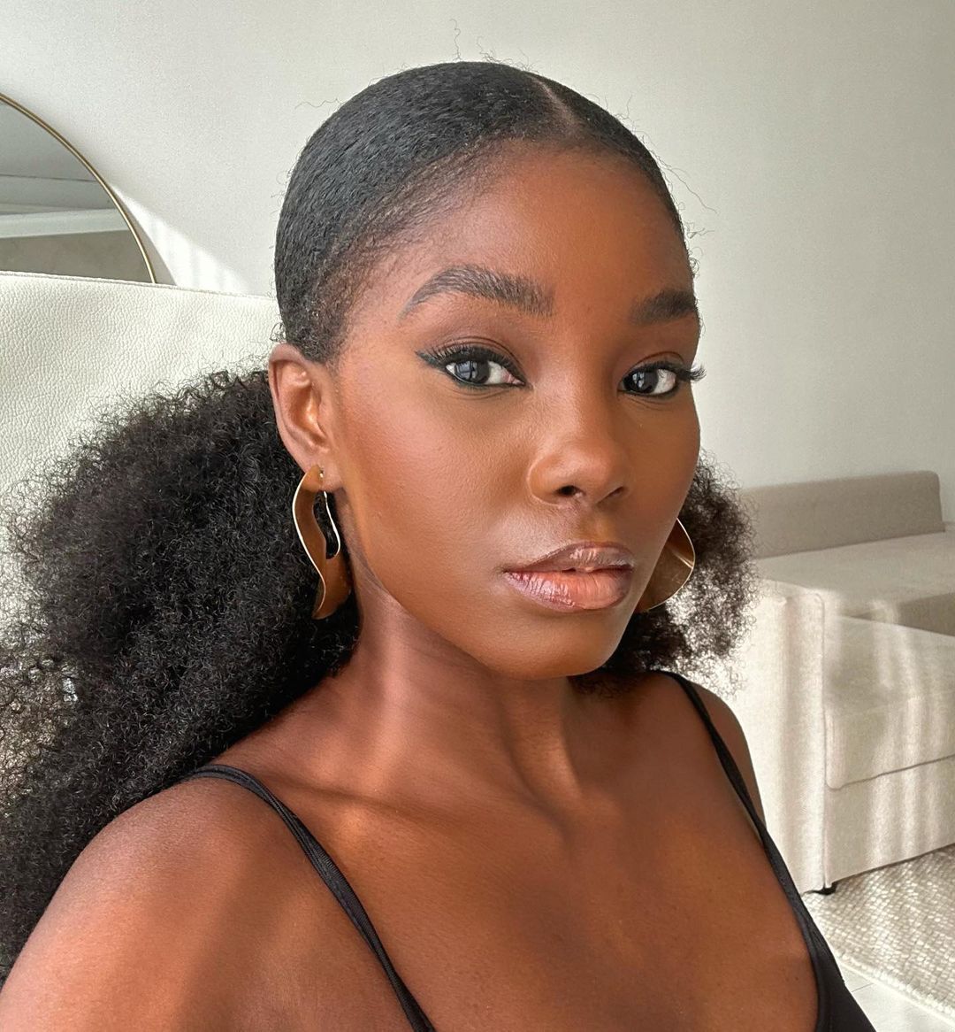 A selfie of woman with curly ponytail and gold earrings.