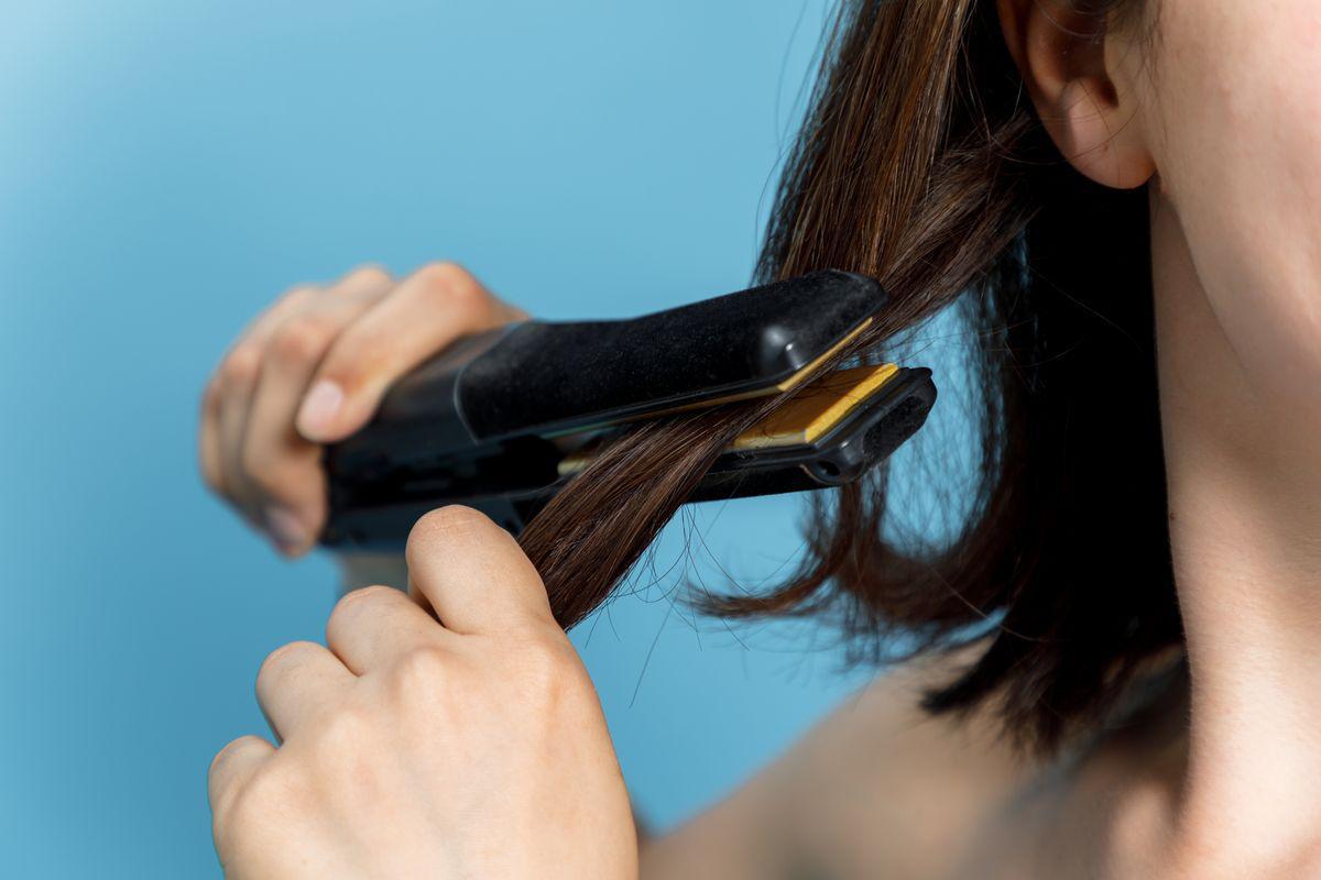 Woman straightening hair with flat iron