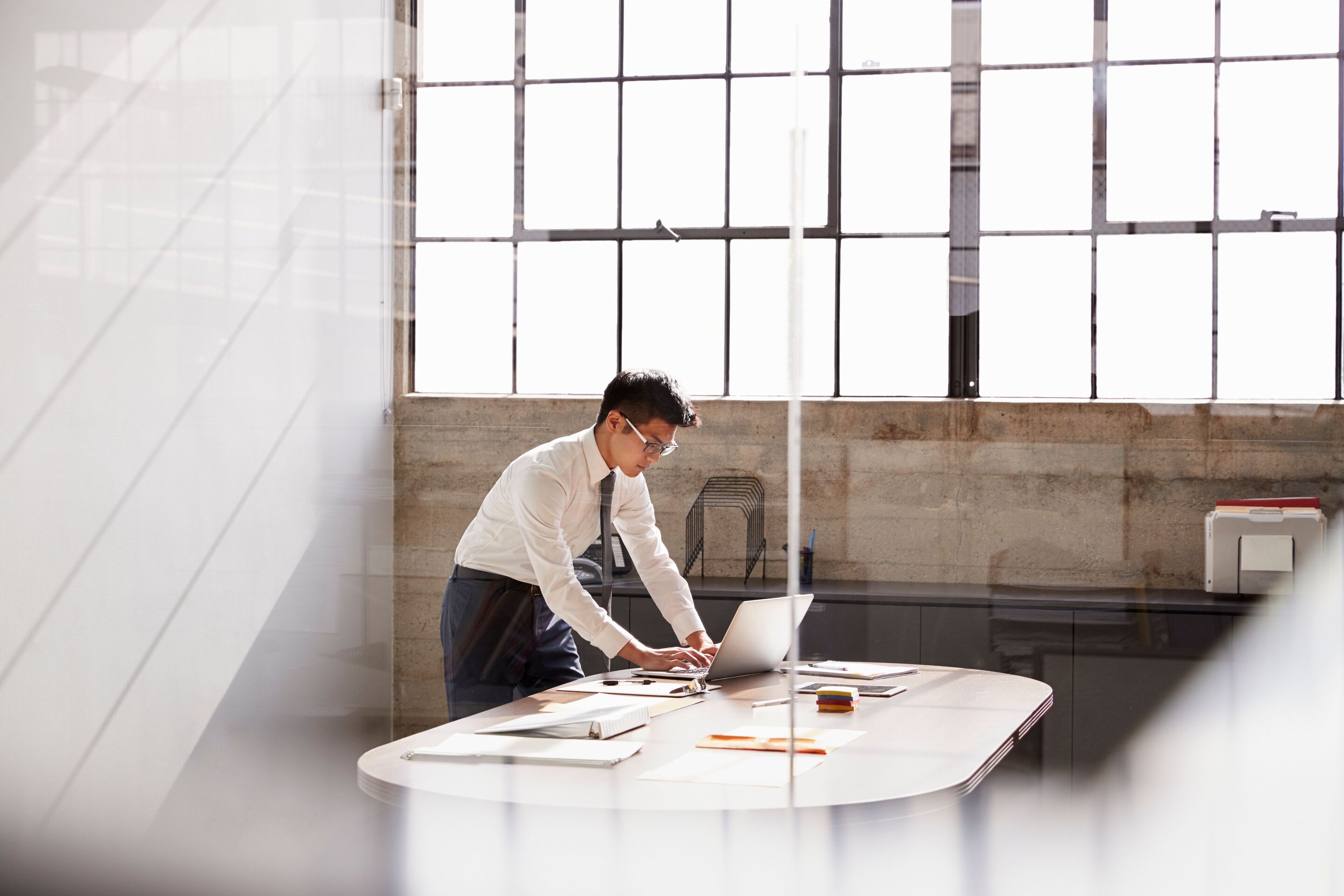 Young Asian man standing over desk with a laptop