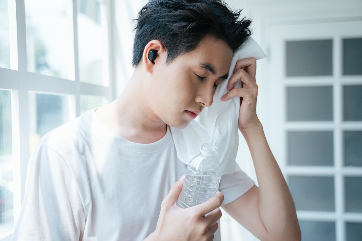 Man in a white shirt holding a bottle of water while wiping his face with a towel.