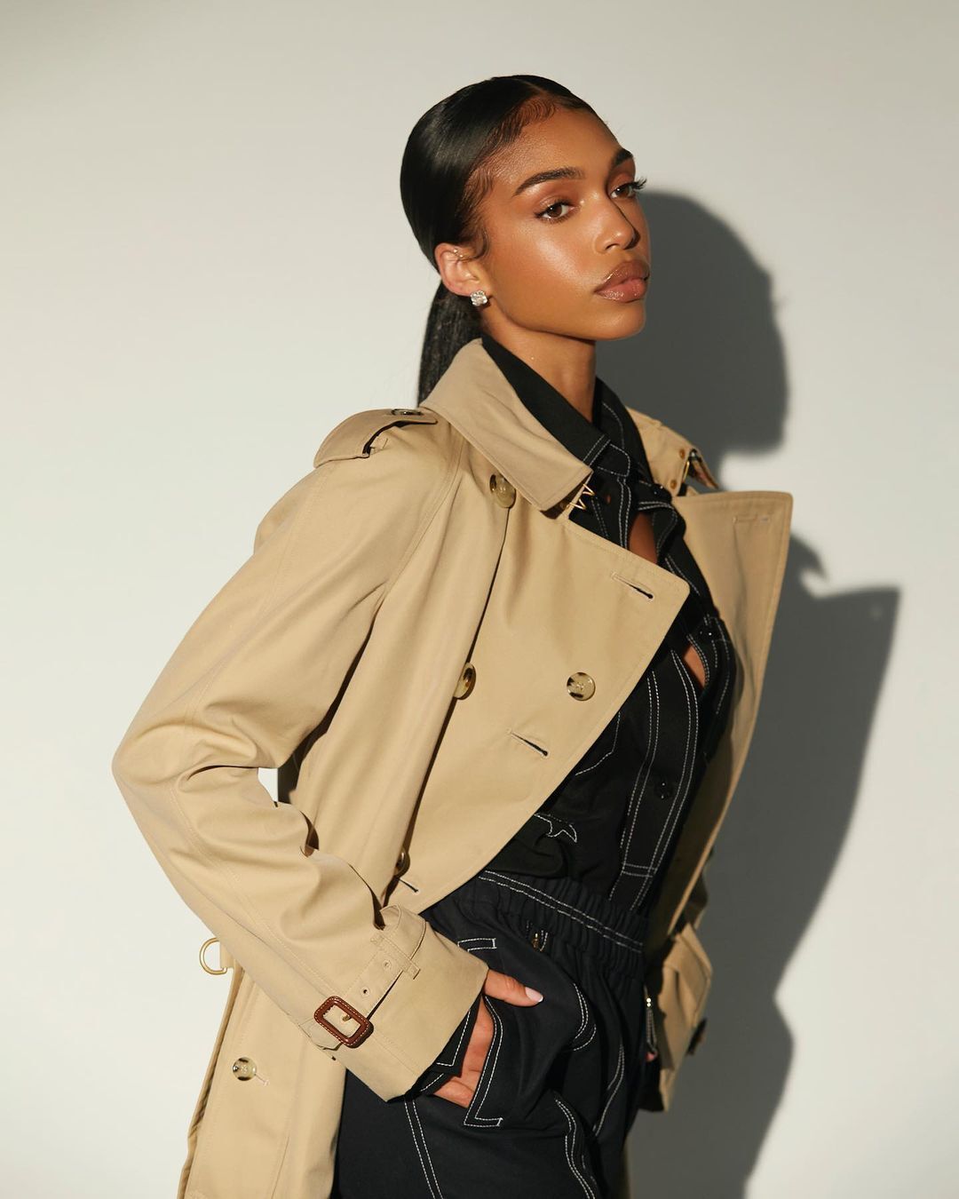 A portrait of Lori Harvey with a sleek ponytail and beige trench coat.