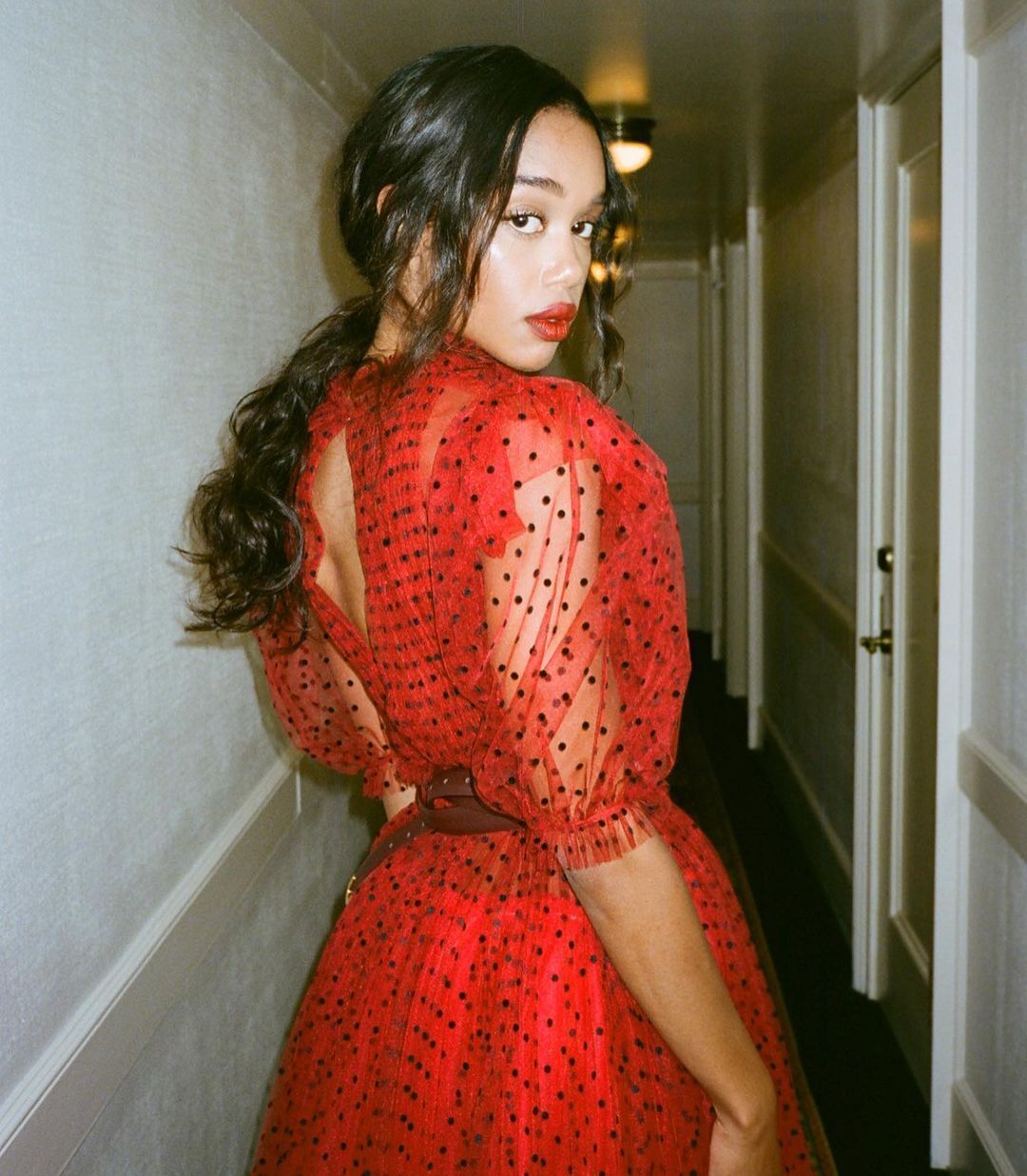 A portrait of Laura Harrier in a red dress wearing a messy ponytail.