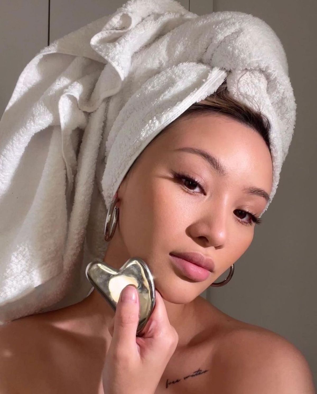 Woman with her hair wrapped in a white towel holding a stainless steel gua sha