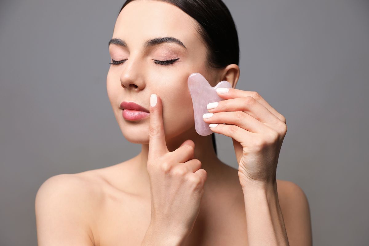 Woman scraping her cheek with a pink rose quartz gua sha.