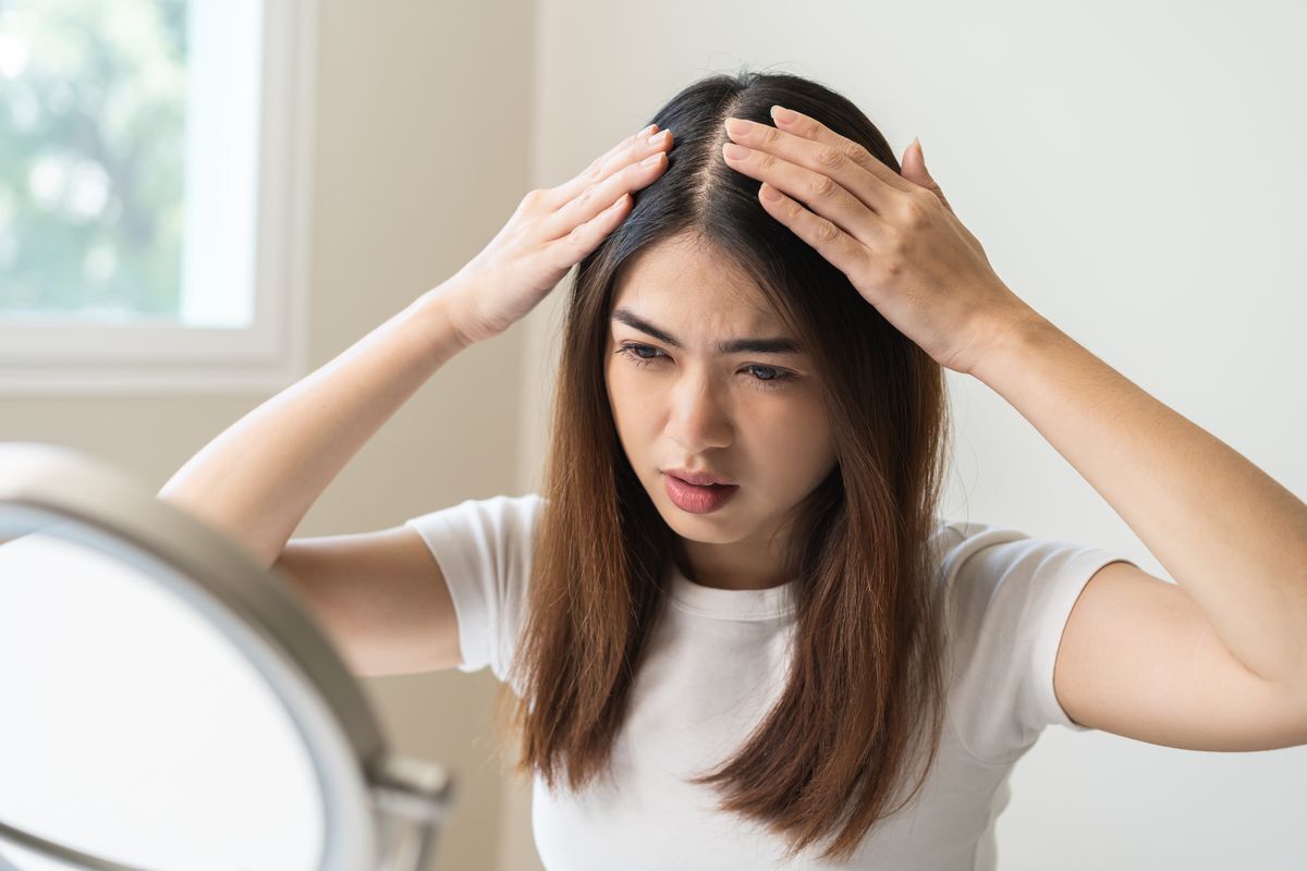Woman looking at her scalp in the mirror.