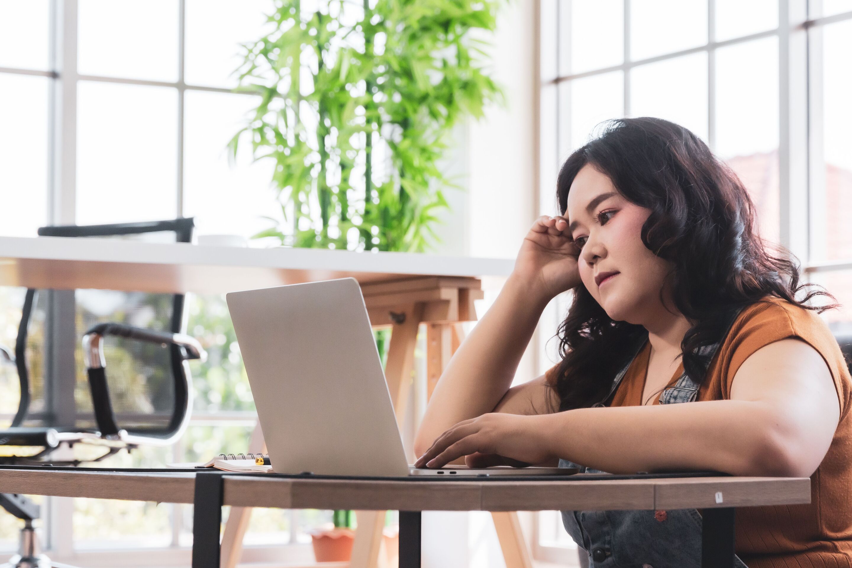 Curvy Asian thinking while looking at laptop