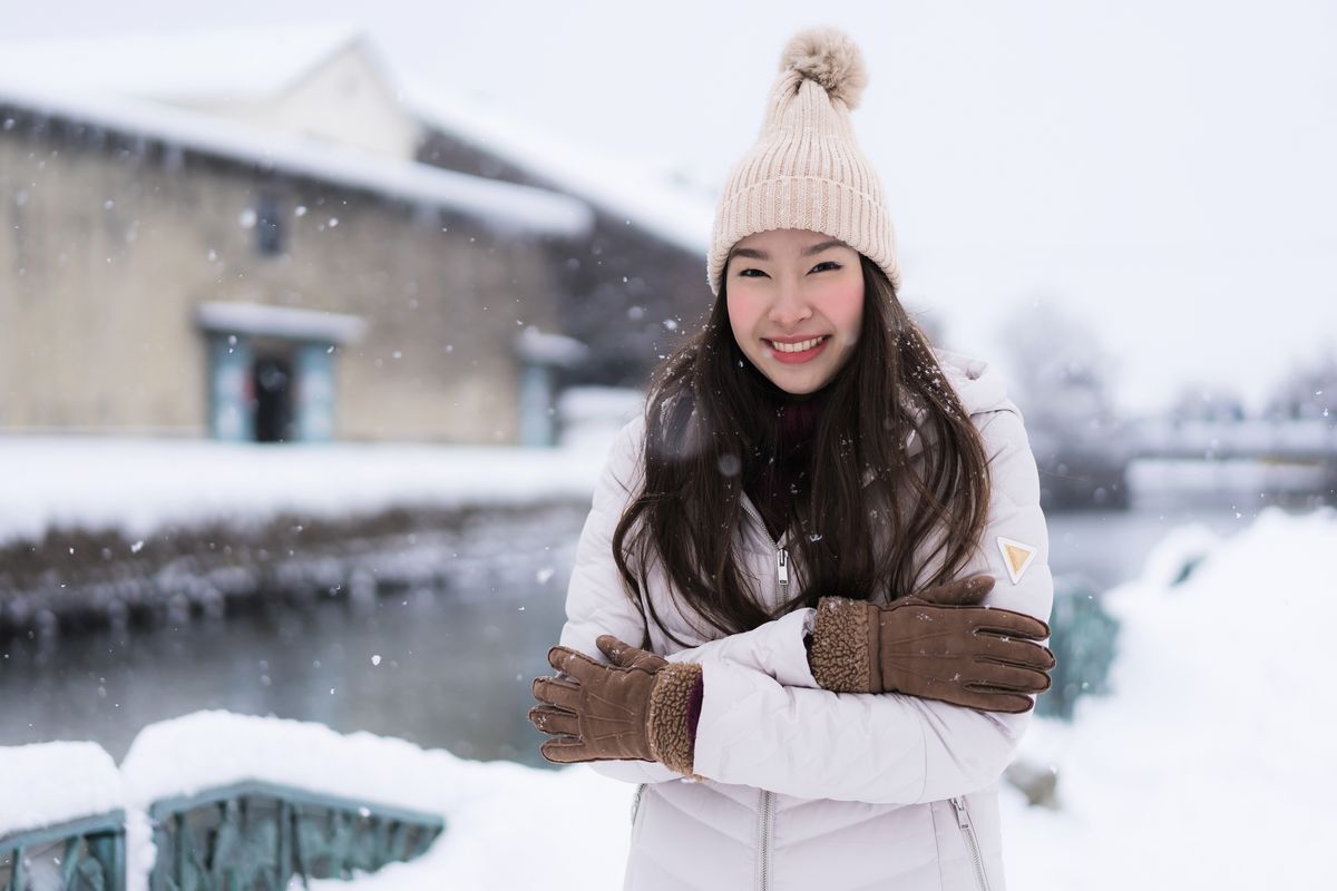 Asian woman wearing a coat, gloves, and a hat out in the snow