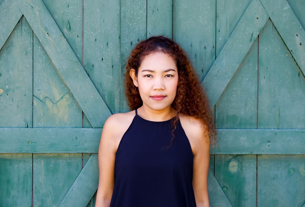 Asian woman with curly hair posing in front of a blue barn door.