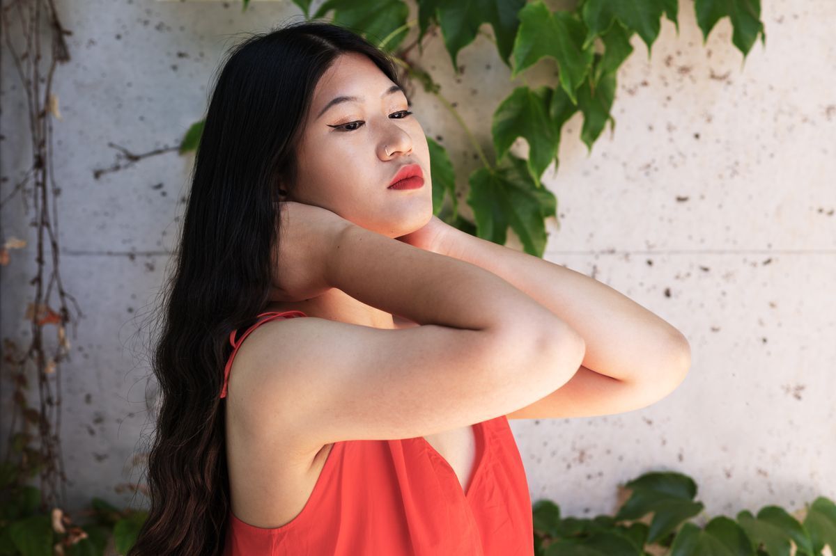 Asian woman in a red top touching her long, black hair.