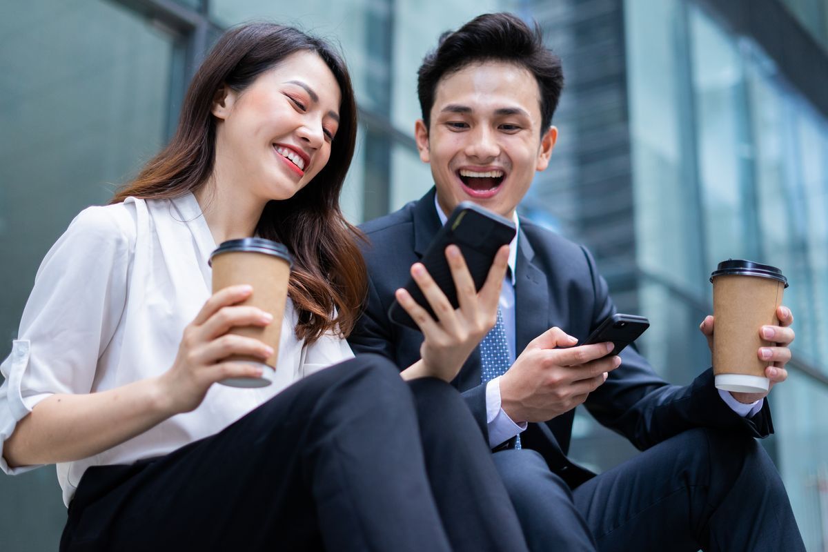 Asian man smiling while looking at female colleague’s phone screen