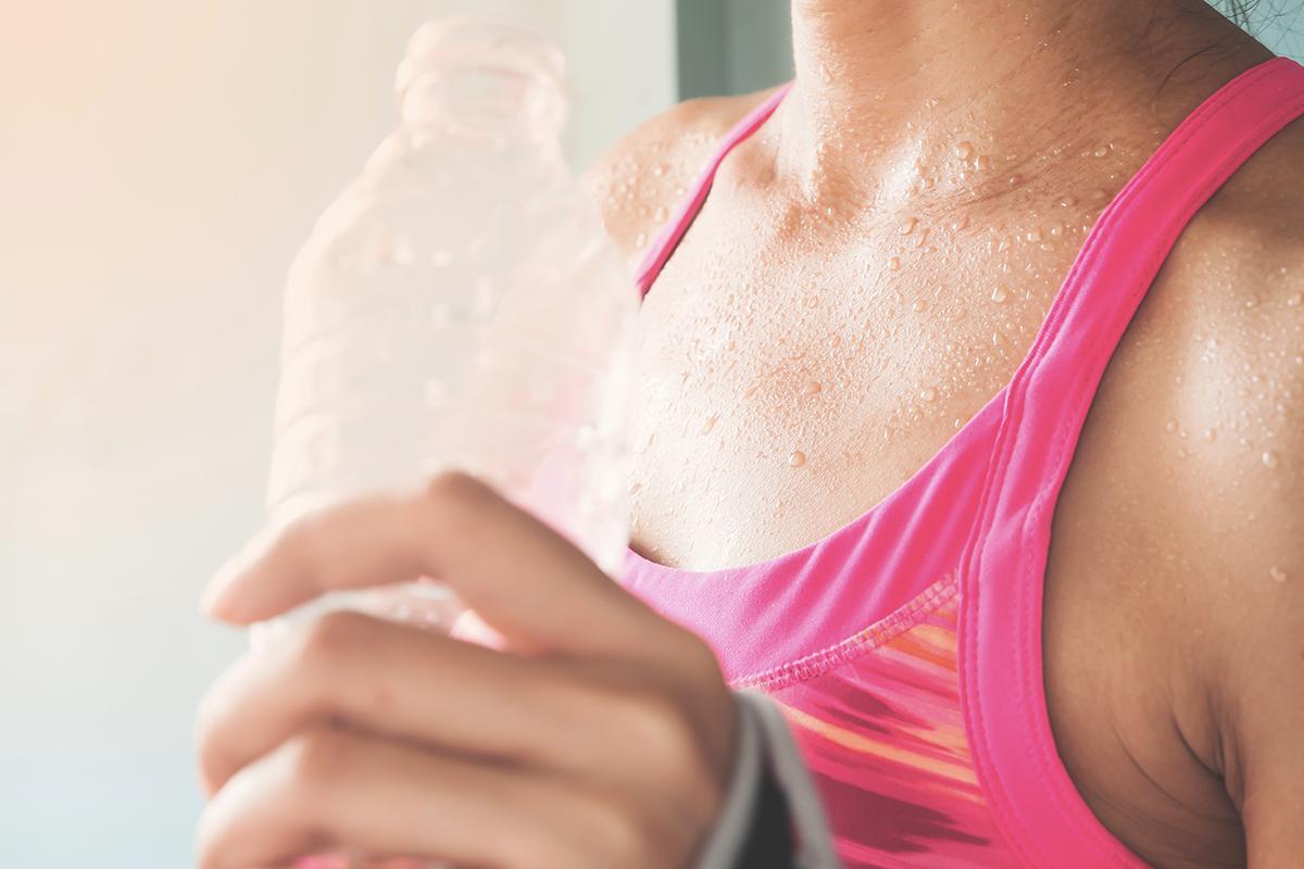 Closeup shot of a woman in a pink fitness top holding a water bottle