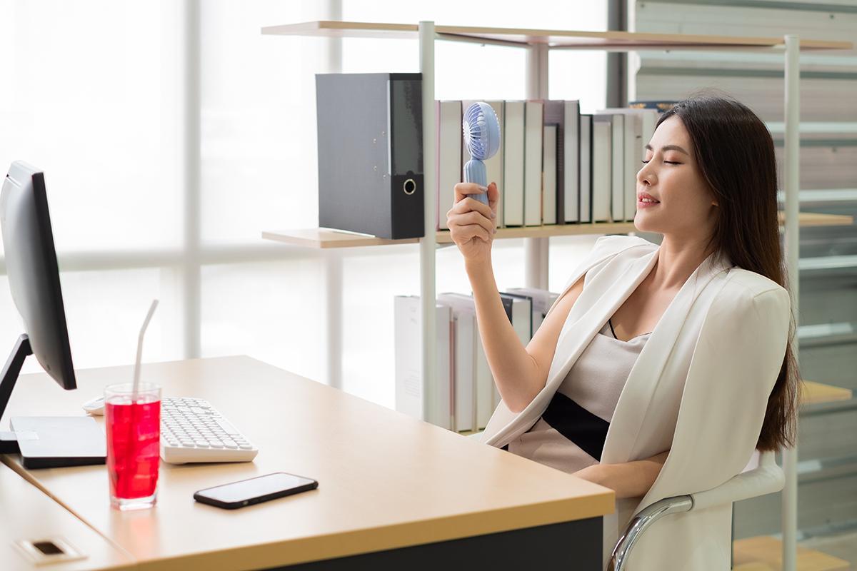 A woman at her desk holding a portable electric fan
