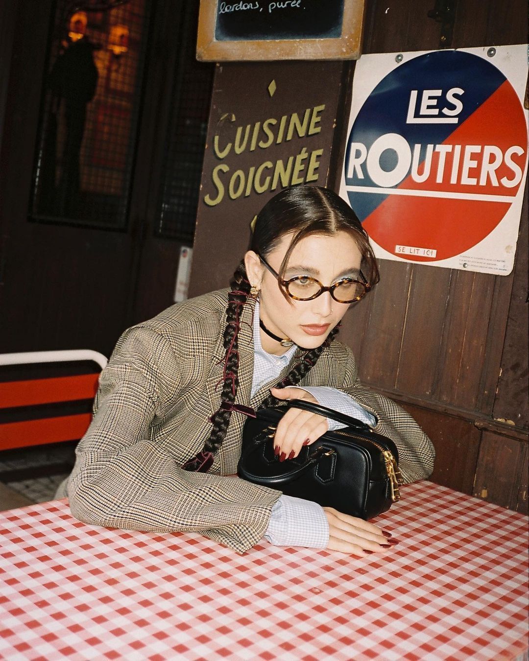 A portrait of Emma Chamberlain with braided pigtails, glasses, and blazer.