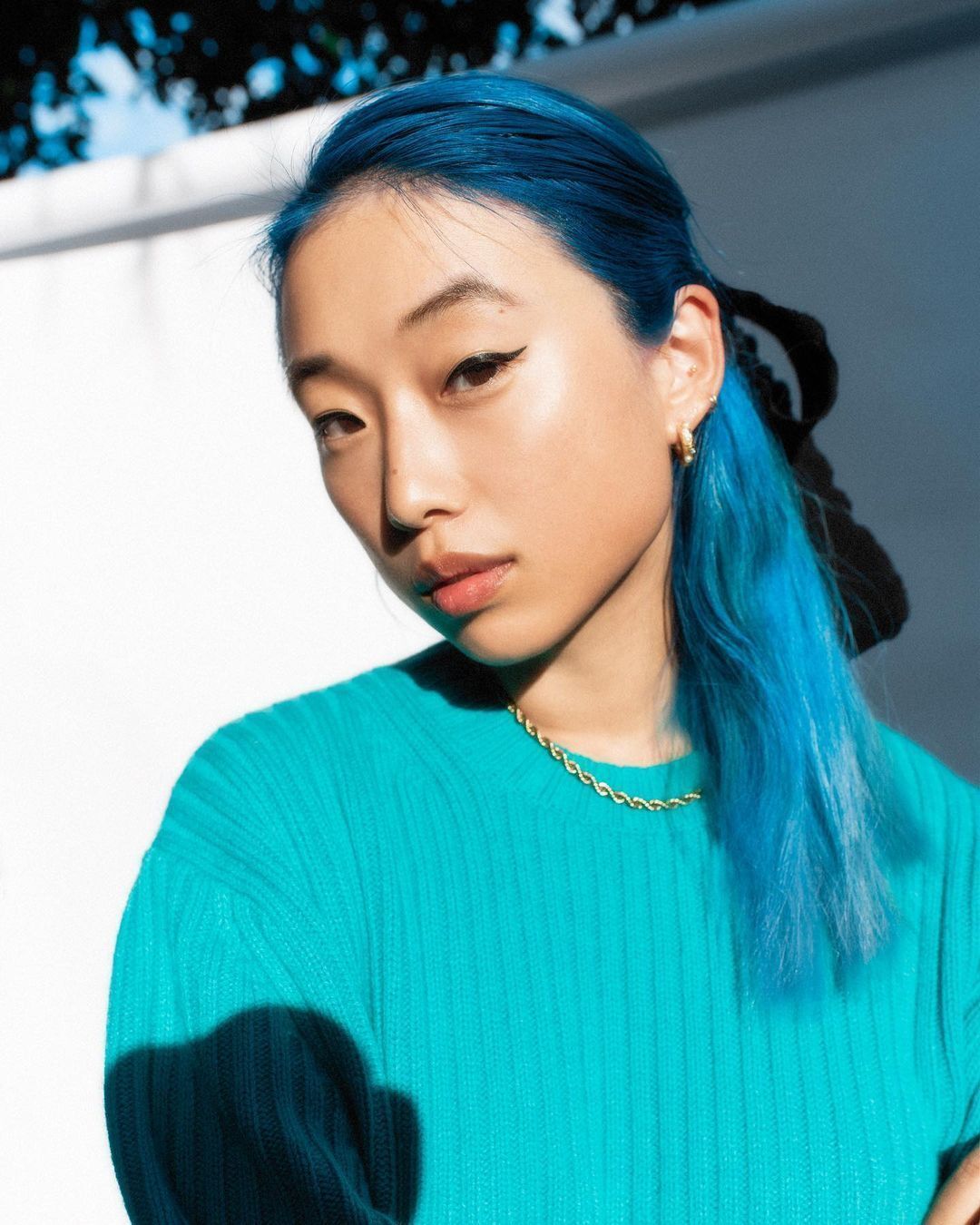 An Asian woman with long blue hair and wearing a blue shirt