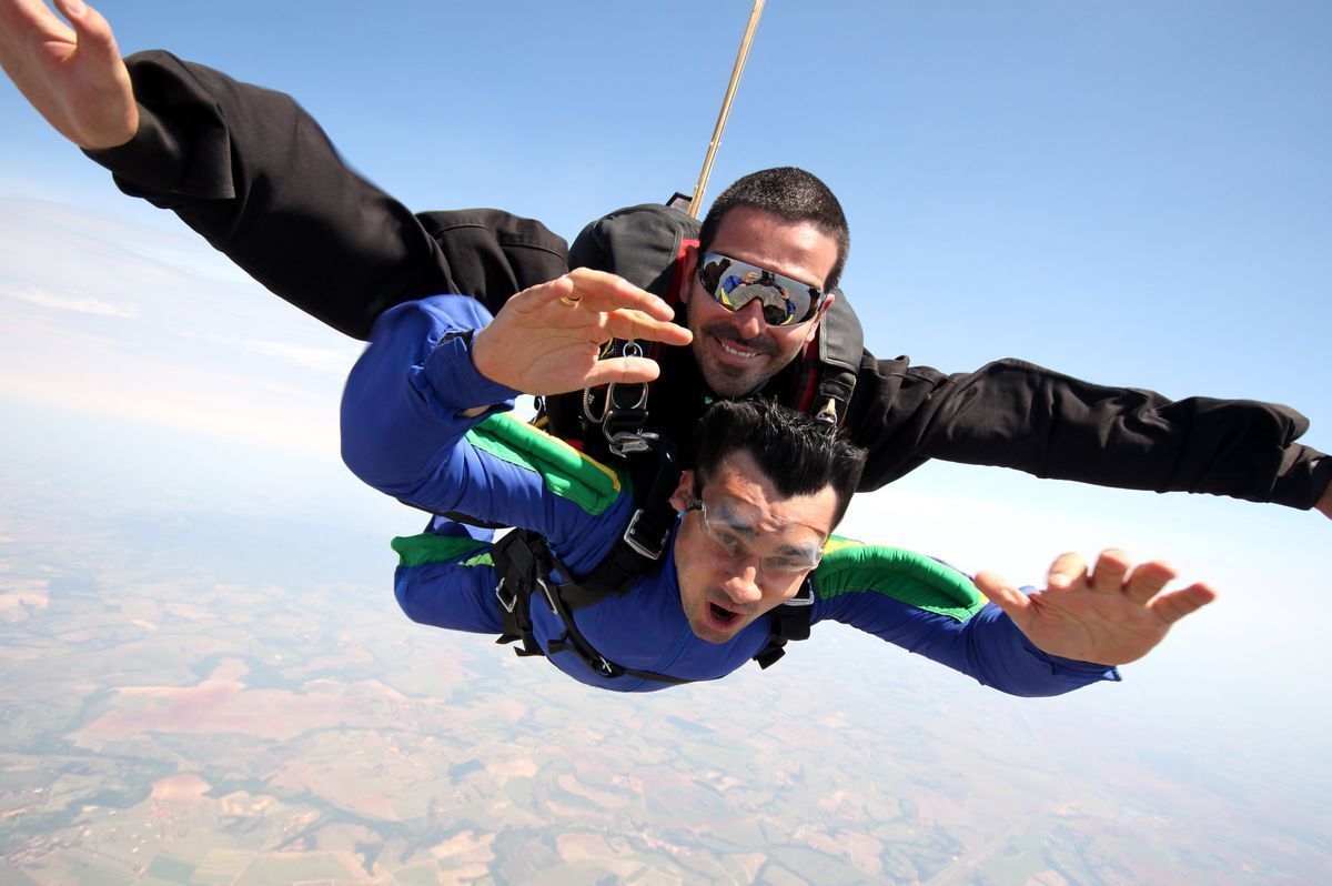 Caucasian man in black and Asian Man in blue skydiving.