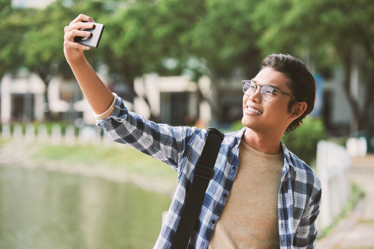 Asian man smiling taking a selfie of himself.