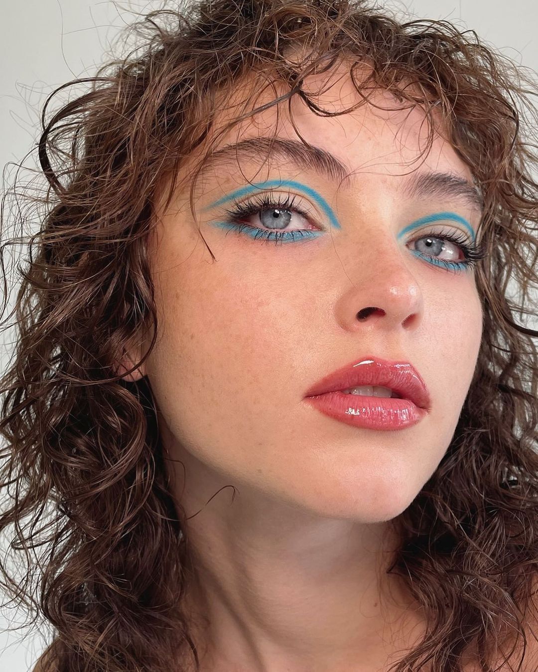 A portrait of woman with blue graphic eyeliner and curly hair.