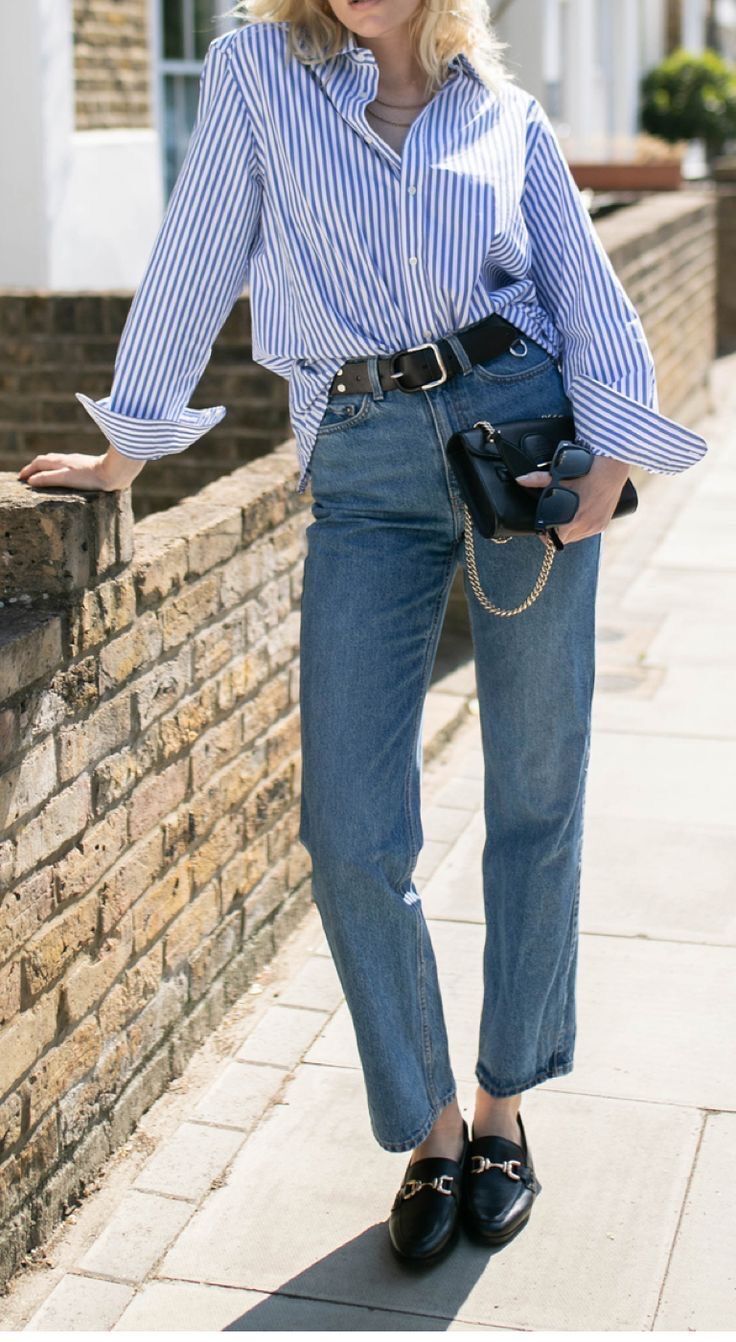 A portrait of woman wearing button down shirt and denim pants.