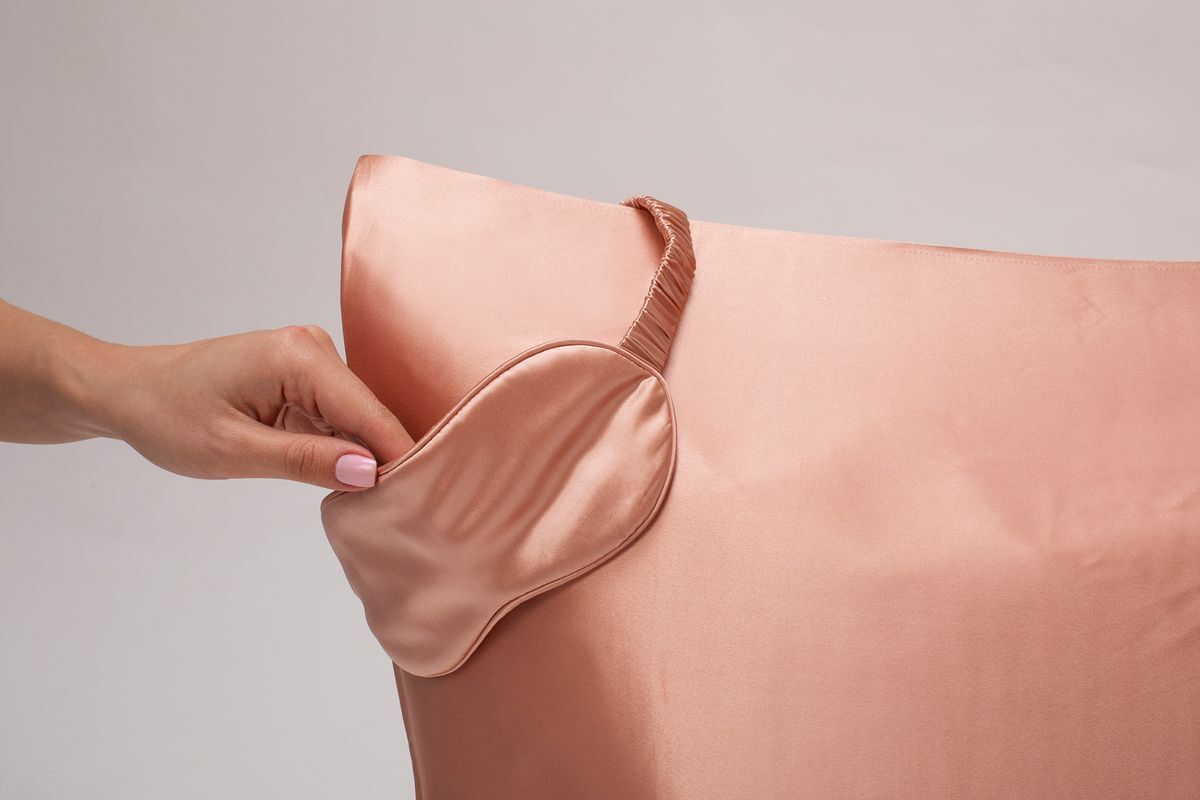 Woman’s hand putting a pink silk sleeping mask over a pink silk pillow.