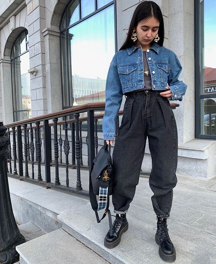 A portrait of woman in black trousers, denim jacket, and gold accessories.