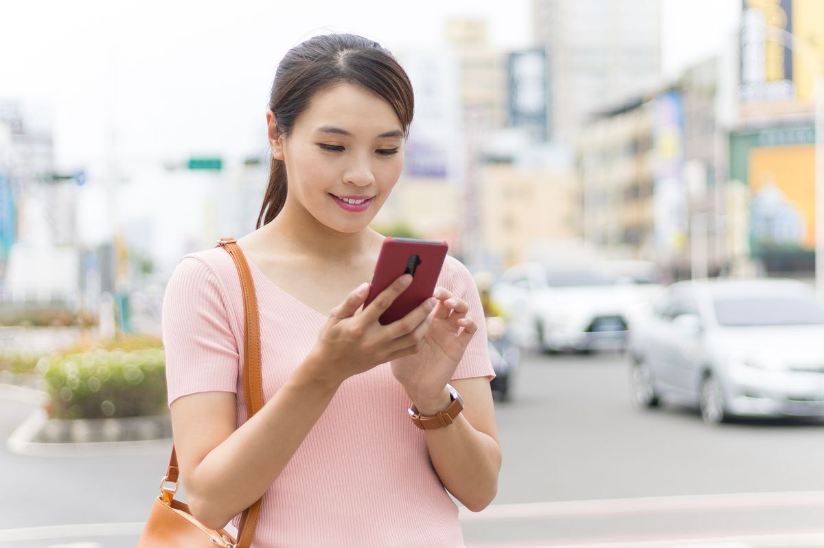 Asian woman with neat hair holding her phone on the street.