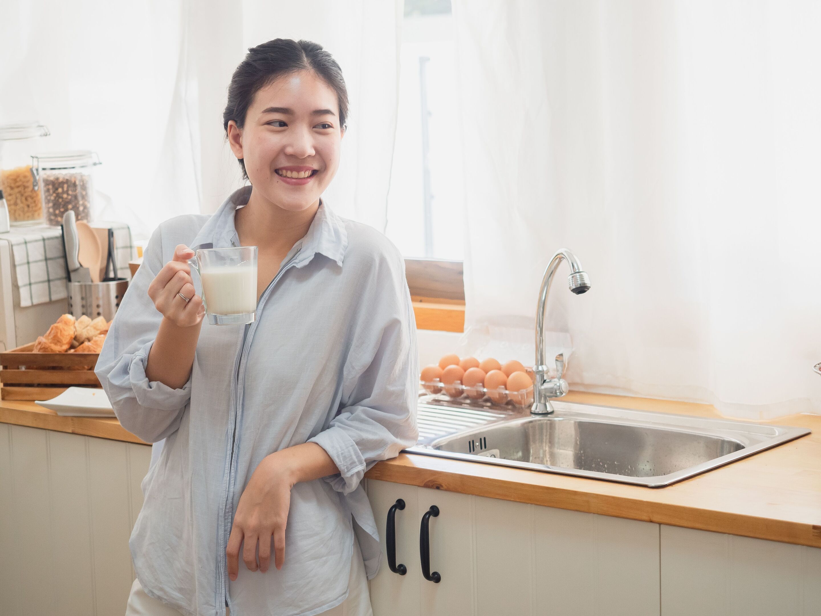 An Asian woman drinking milk by the kitchen sink