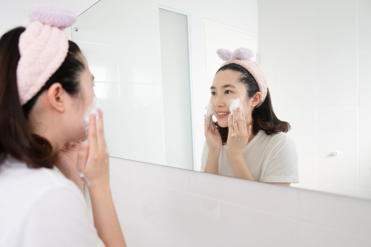 Asian woman wearing a headband while washing her face.