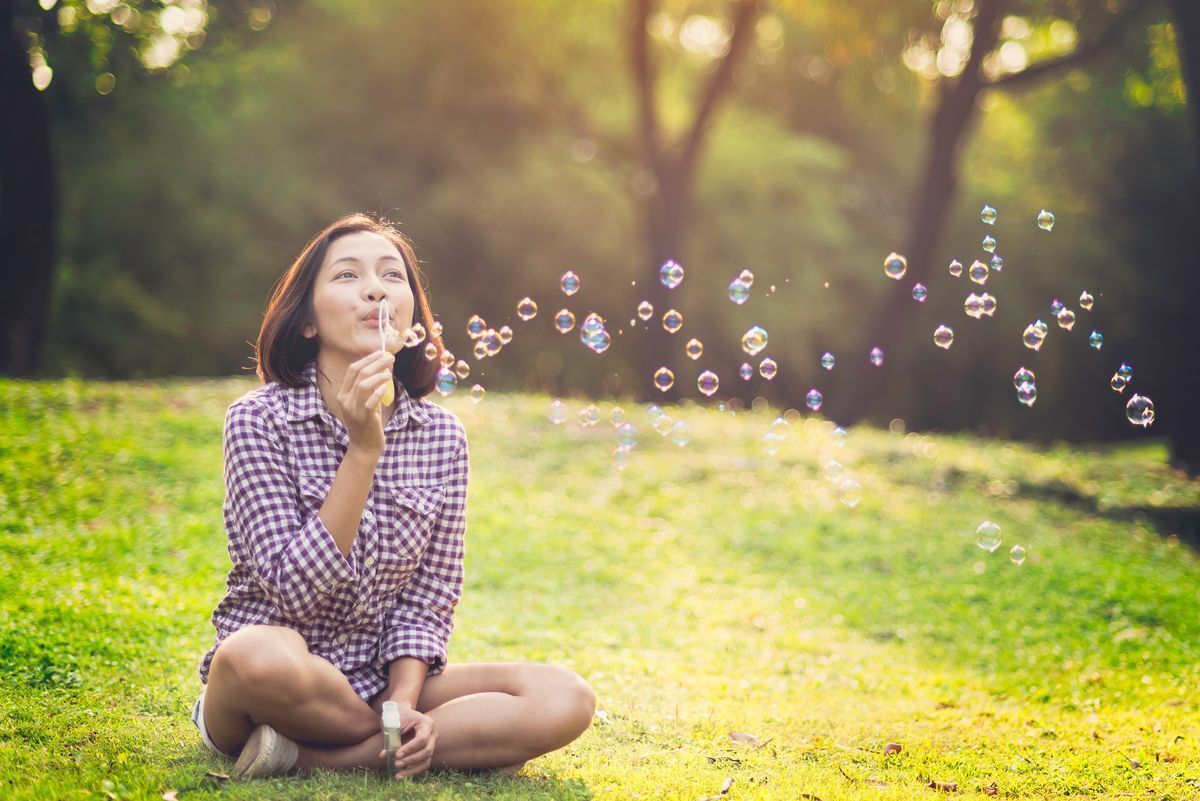 Asian woman blowing bubbles while sitting on the grass