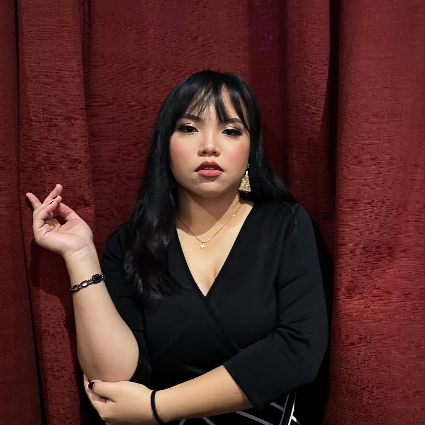 Fierce Asian woman with black hair and bangs posing against a red curtain. 