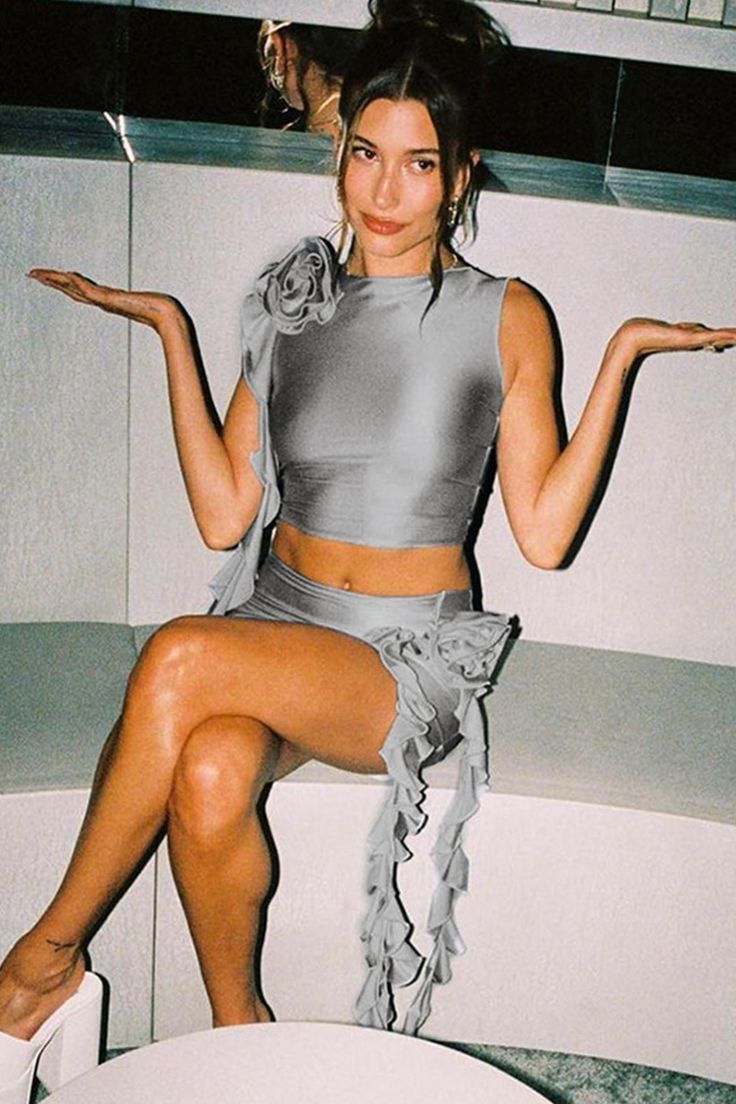 A portrait of Hailey Bieber wearing silver crop top and skirt with rosette decoration.
