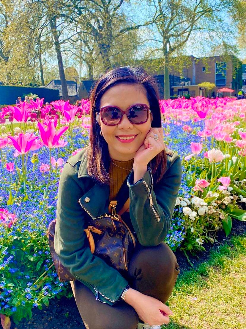 Asian woman in sunglasses kneeling by a bed of flowers.
