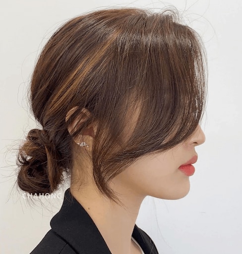 Side view of an Asian woman with a messy bun against a white background.
