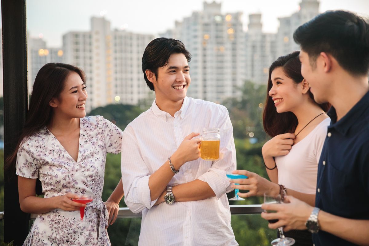 Asian man holding a beer at a party with friends.