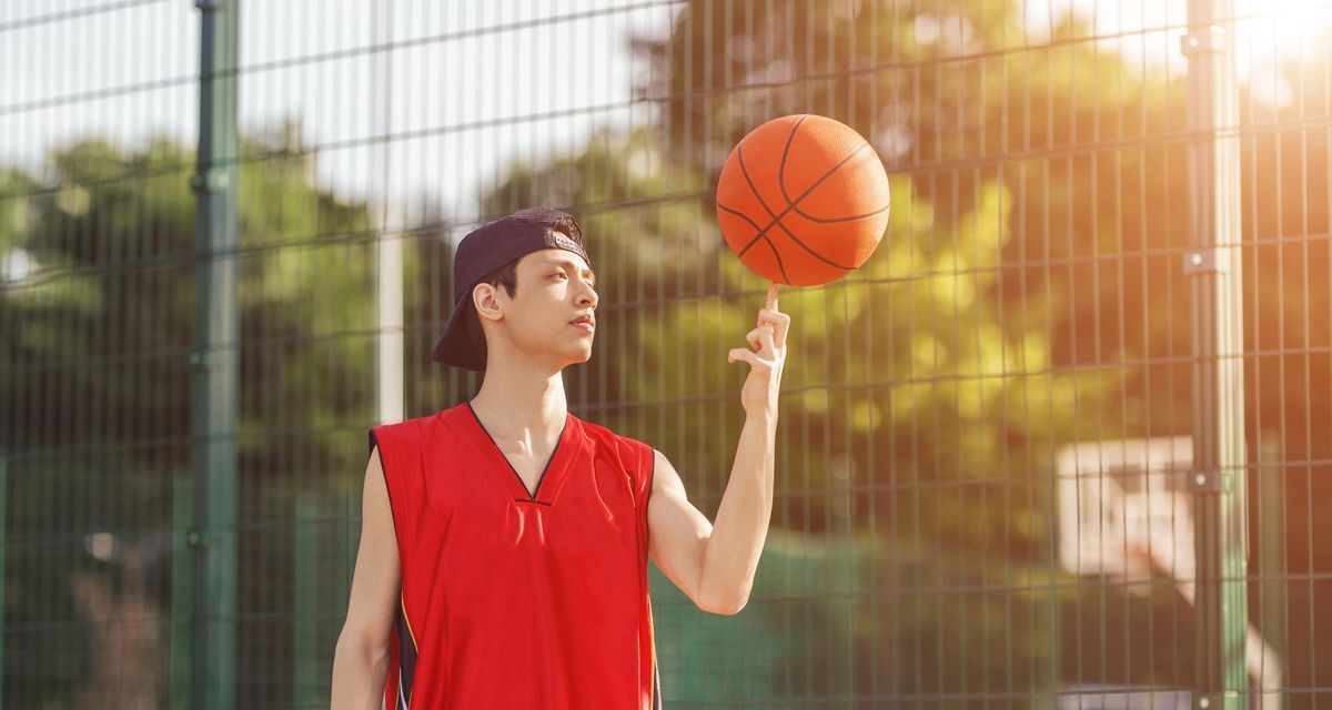 Asian man playing basketball outdoors.