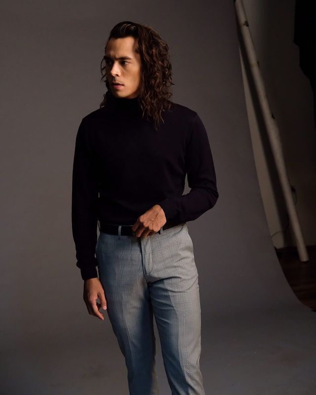 Jake Cuenca with long combover hairstyle, black turtleneck, and gray slacks. 