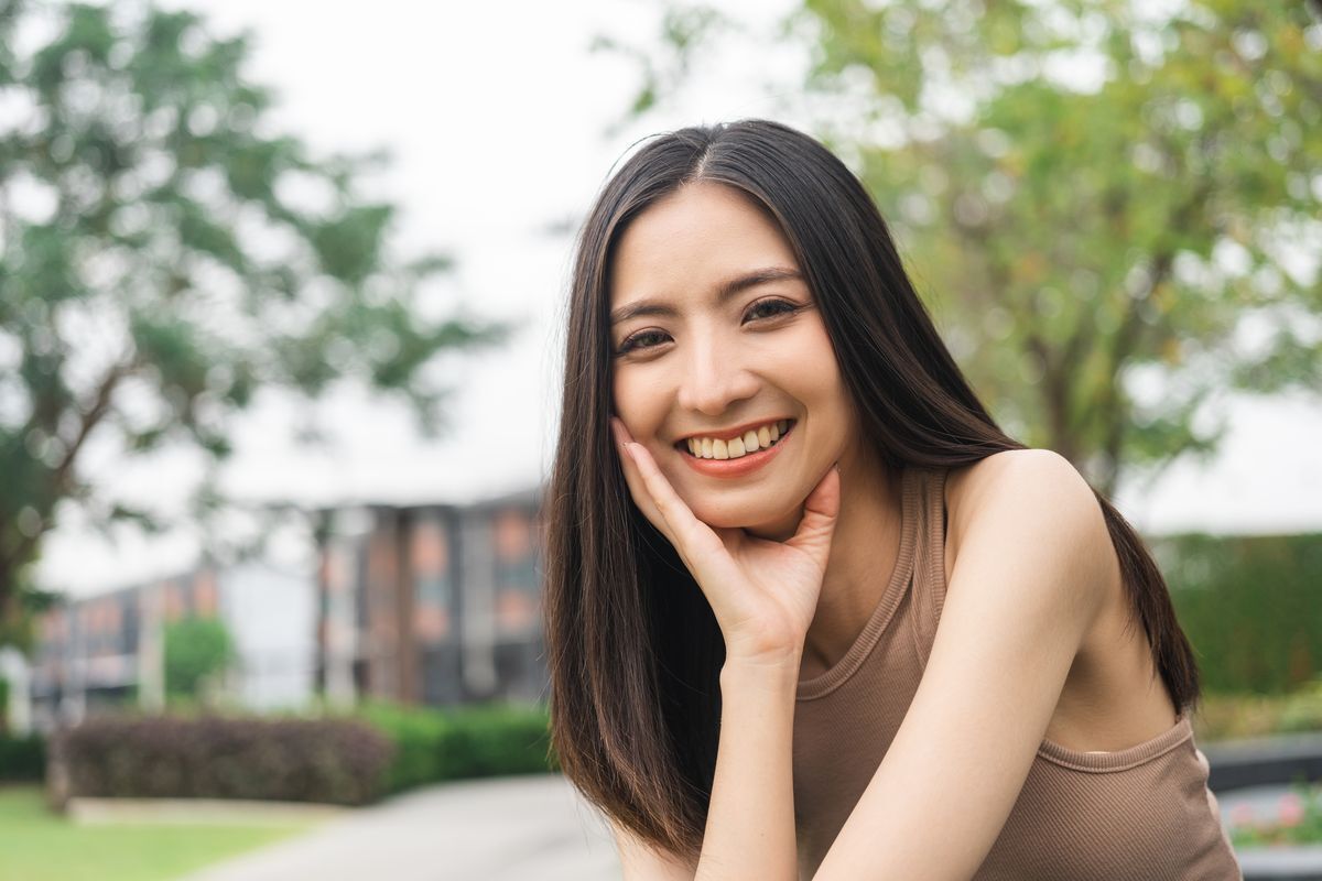 Woman in a brown top sitting at a park and smiling at the camera.