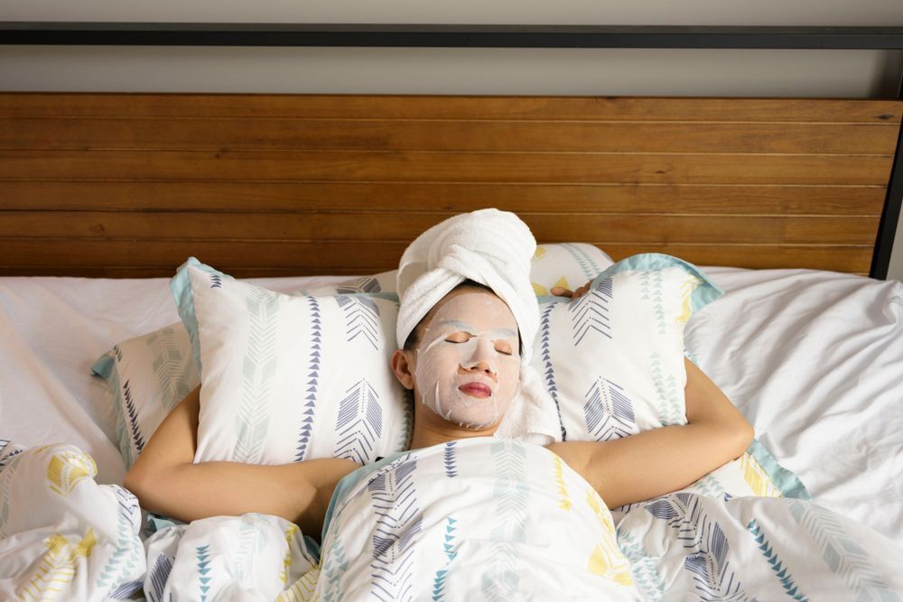 Woman sleeping on her bed with sheet mask on her face.