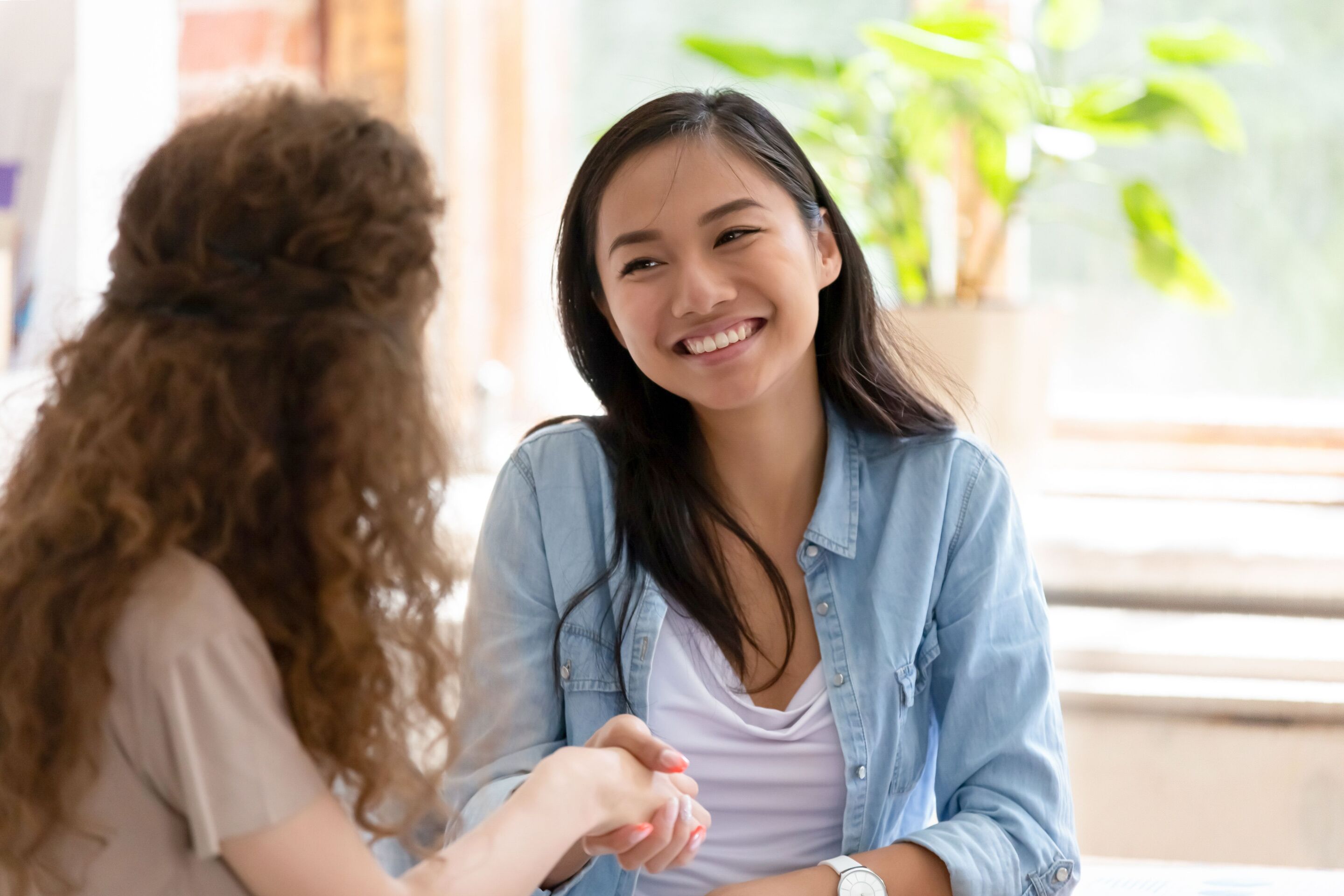 Asian woman in denim jacket shaking hands with a woman with curly hair