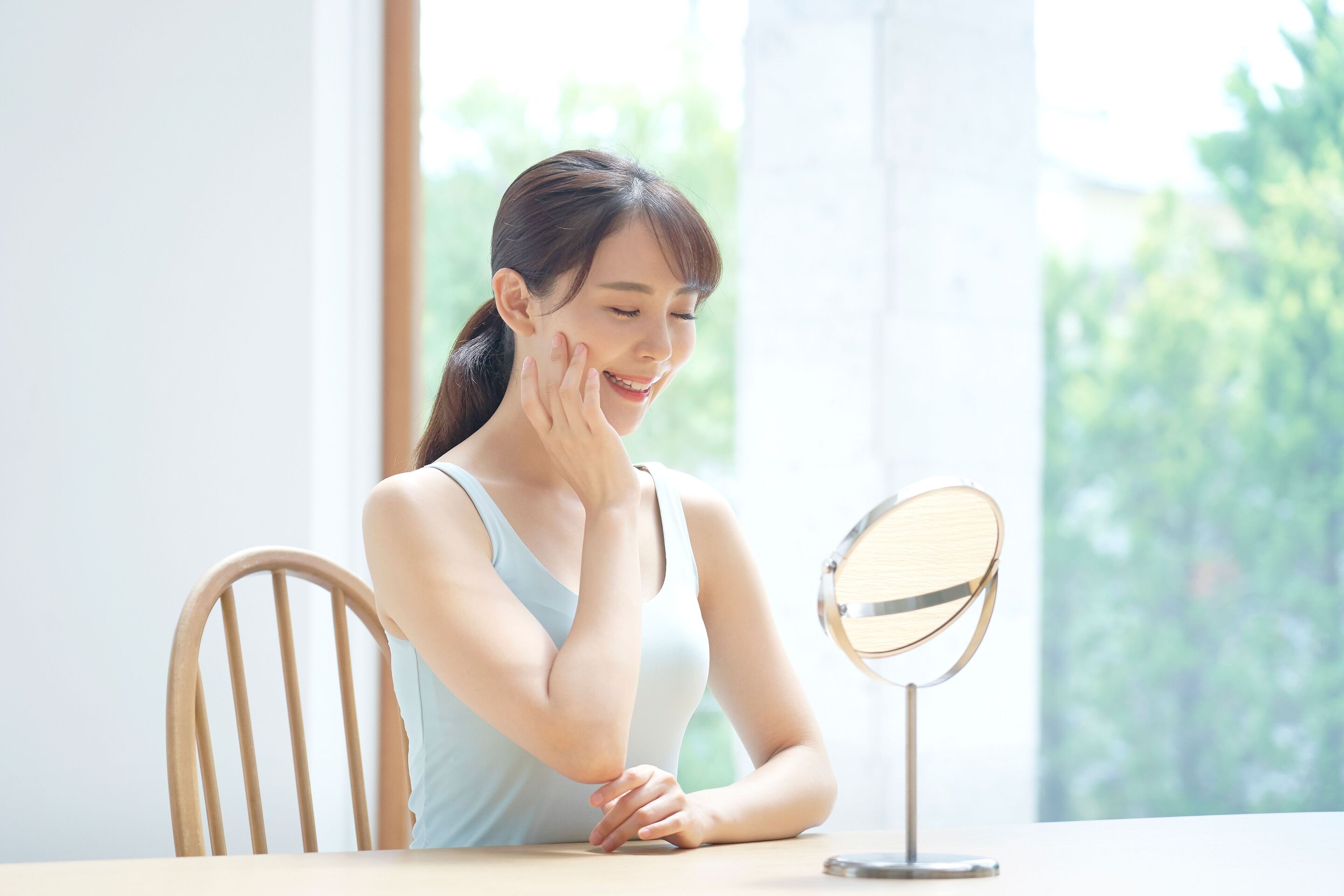 An Asian woman smiling and touching her face
